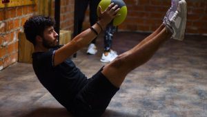 Focused man performing core exercises with a medicine ball in an indoor gym highlighting fitness and strength.